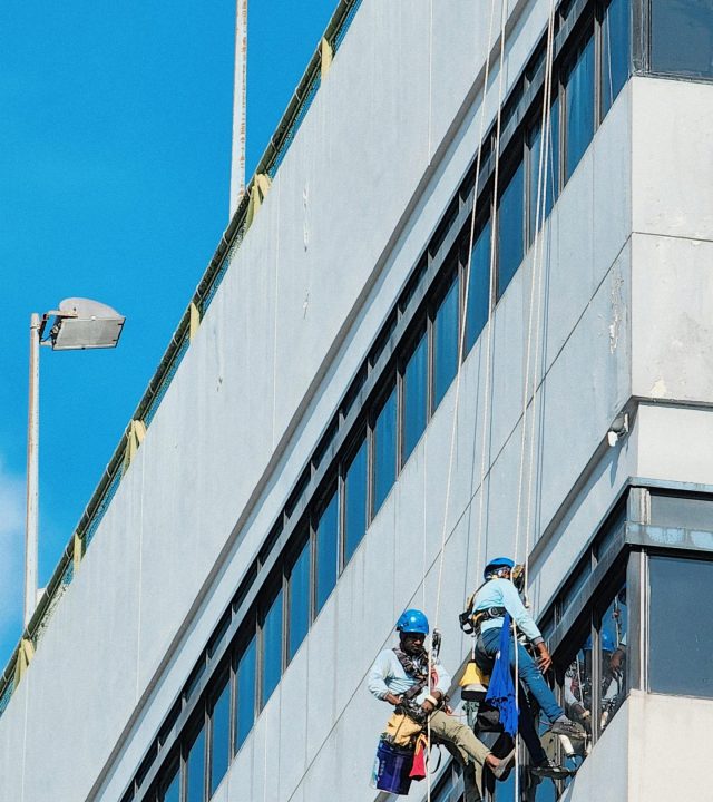 Professional window cleaners safely suspended on the facade of a modern building in Singapore.